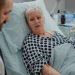 Close up elder patient laying bed talking medic healthcare treatment doctor consulting sick woman with nasal oxygen tube iv drip bag recovery hospital ward