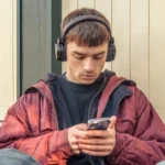 Young man listens music headphones looks phone