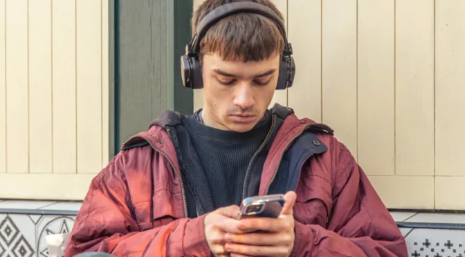 Young man listens music headphones looks phone